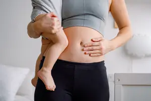 woman pressing on her c-section shelf while holding her baby